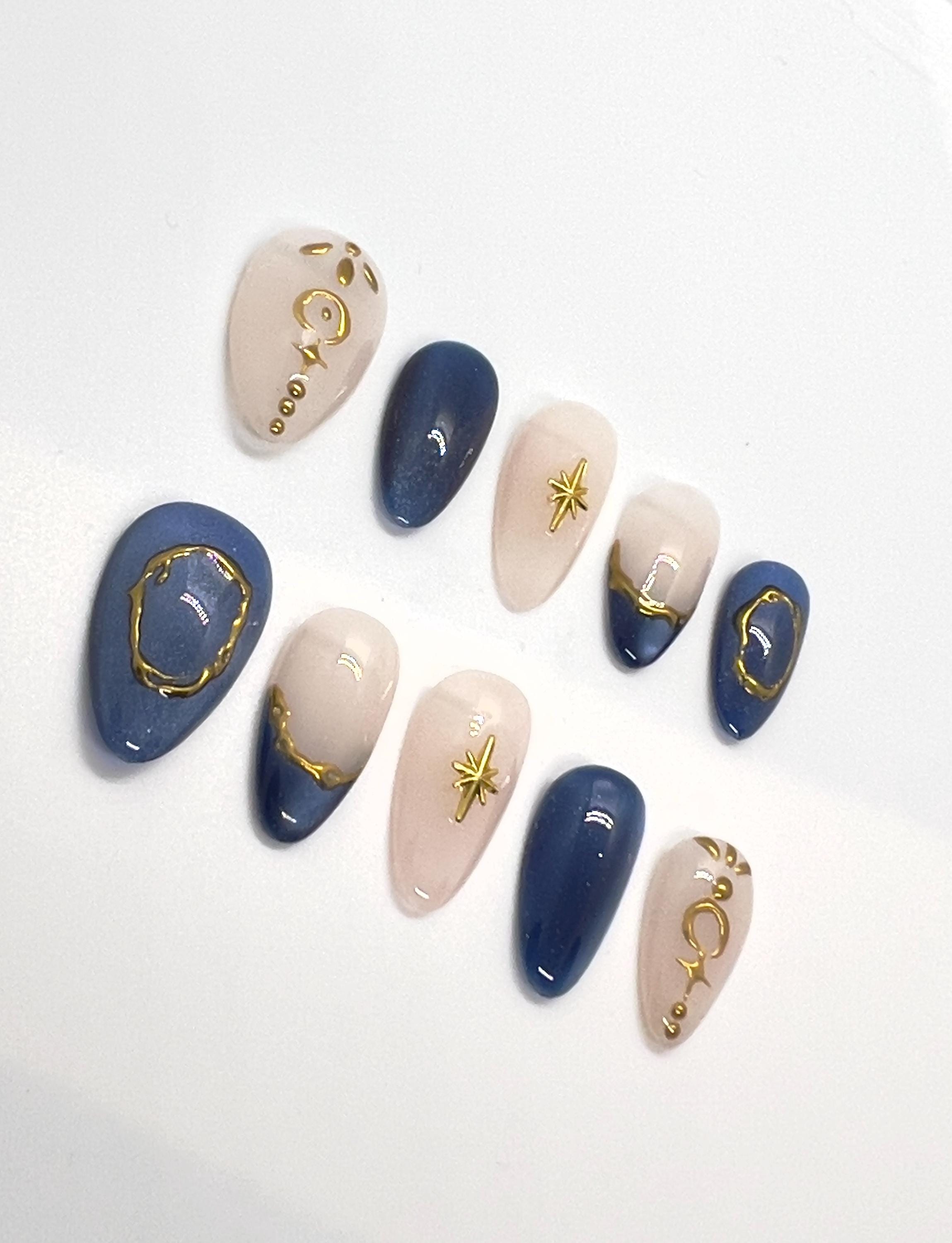 Handmade press-on nails featuring blue, beige, and gold designs on a white background