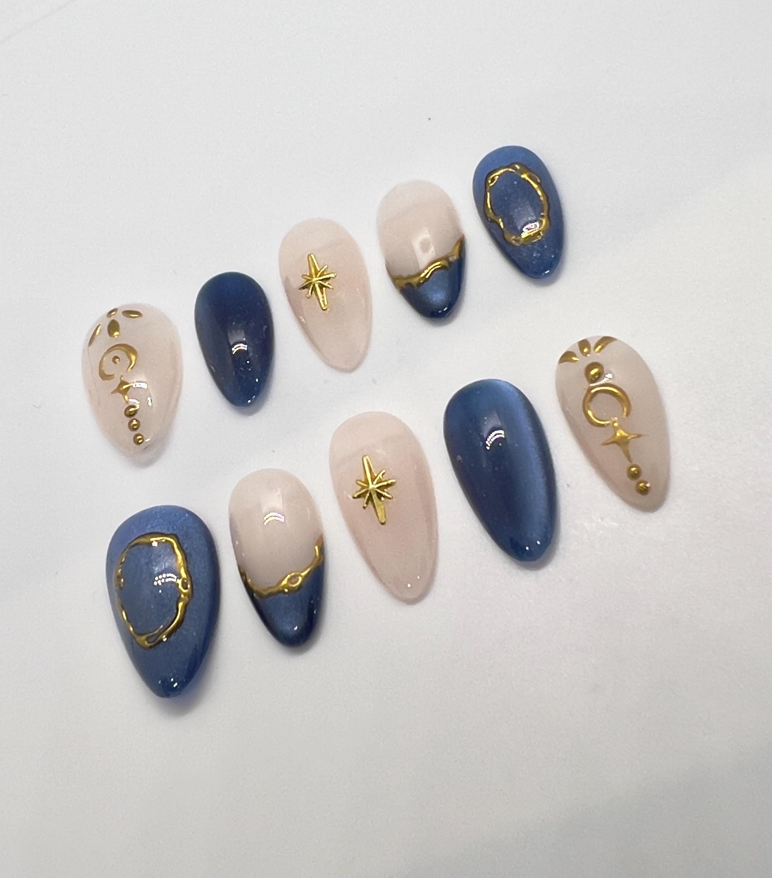 Handmade press-on nails featuring blue, beige, and gold designs on a white background